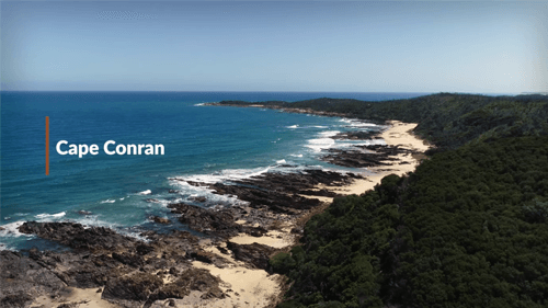 Cape Conran beach, the ocean is blue on the right surrounded by a rocky-sandy beach with that leads into a lush green forest