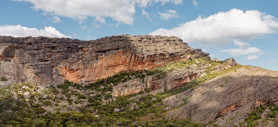 The big orange cliffs of Gunigalg, Gariwerd (Grampians) surrounded by green trees and blue sky