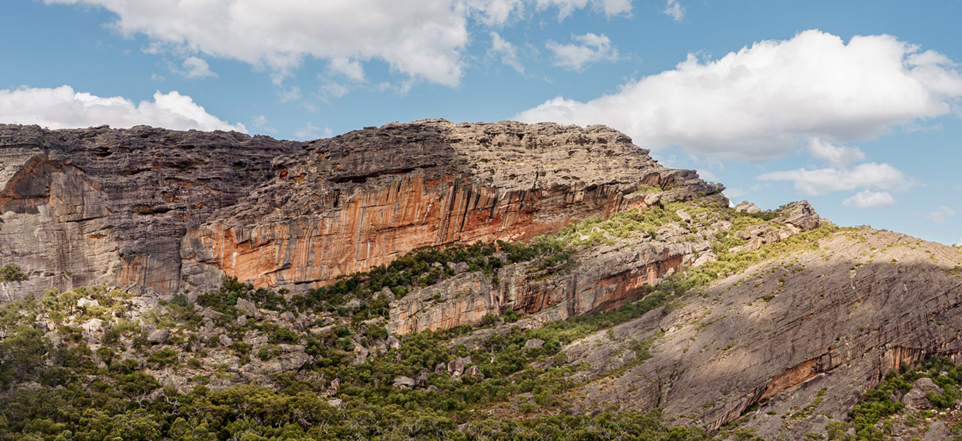 The big orange cliffs of Gunigalg, Gariwerd (Grampians) surrounded by green trees and blue sky