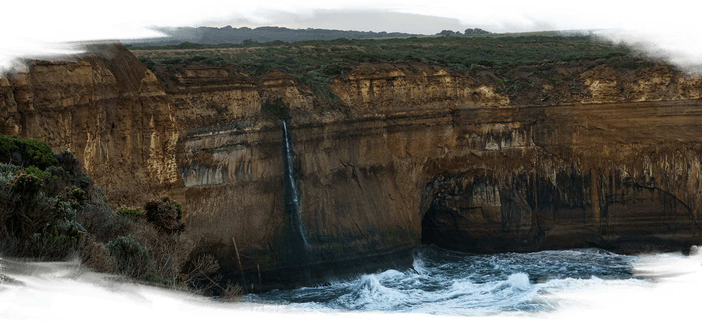 A thin silver waterfall falling off gigantic cliffs and into the ocean at the Great Ocean Rd - Eastern Maar and Wadawurrung Country
