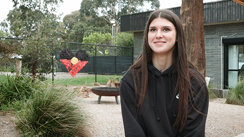 Jira Nelson outdoors at school with an Aboriginal Flag heart in the background