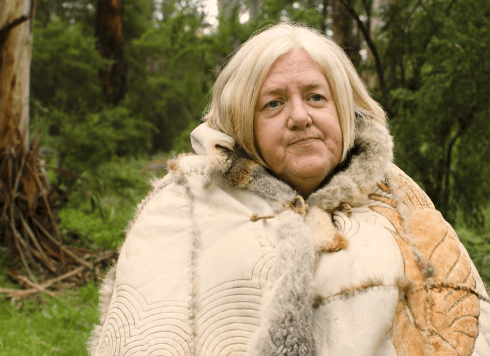 Aunty Diane-Kerr wearing a possum skin cloak with green bush and gum trees in the background