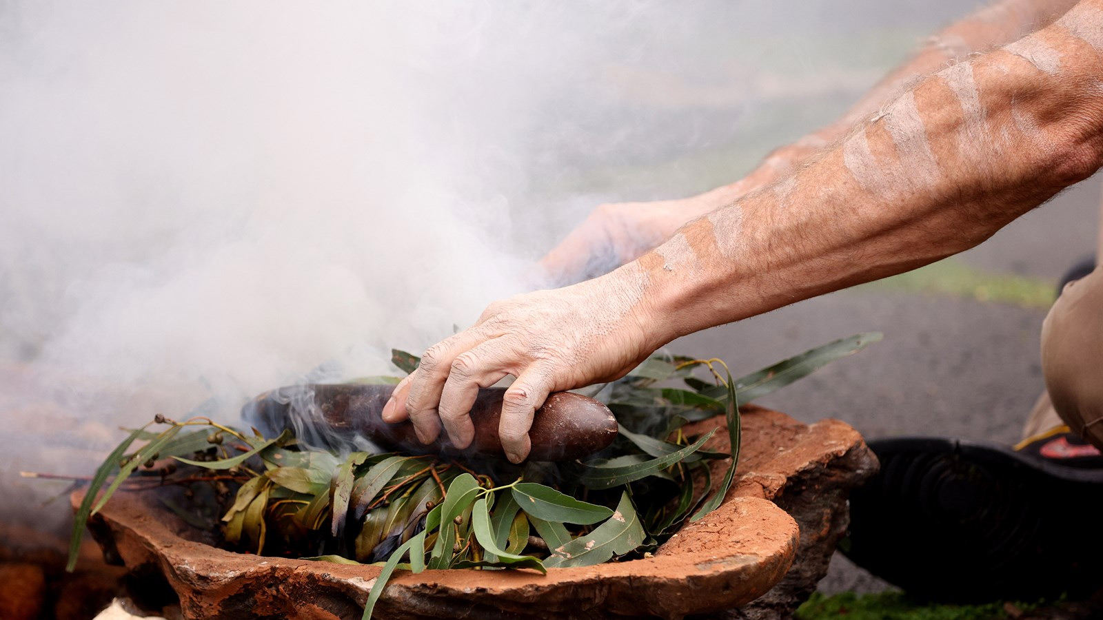 Close up hands performing a smoking ceremony at a Welcome to Country.