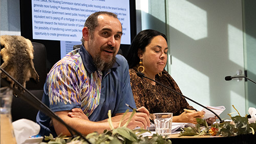 Rueben Berg in-front of a microphone discussing the difficulties of compounding injustices First People face at a public hearing. With Ngarra Murray in the background.